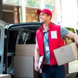A man in red vest holding a box and standing next to a van.